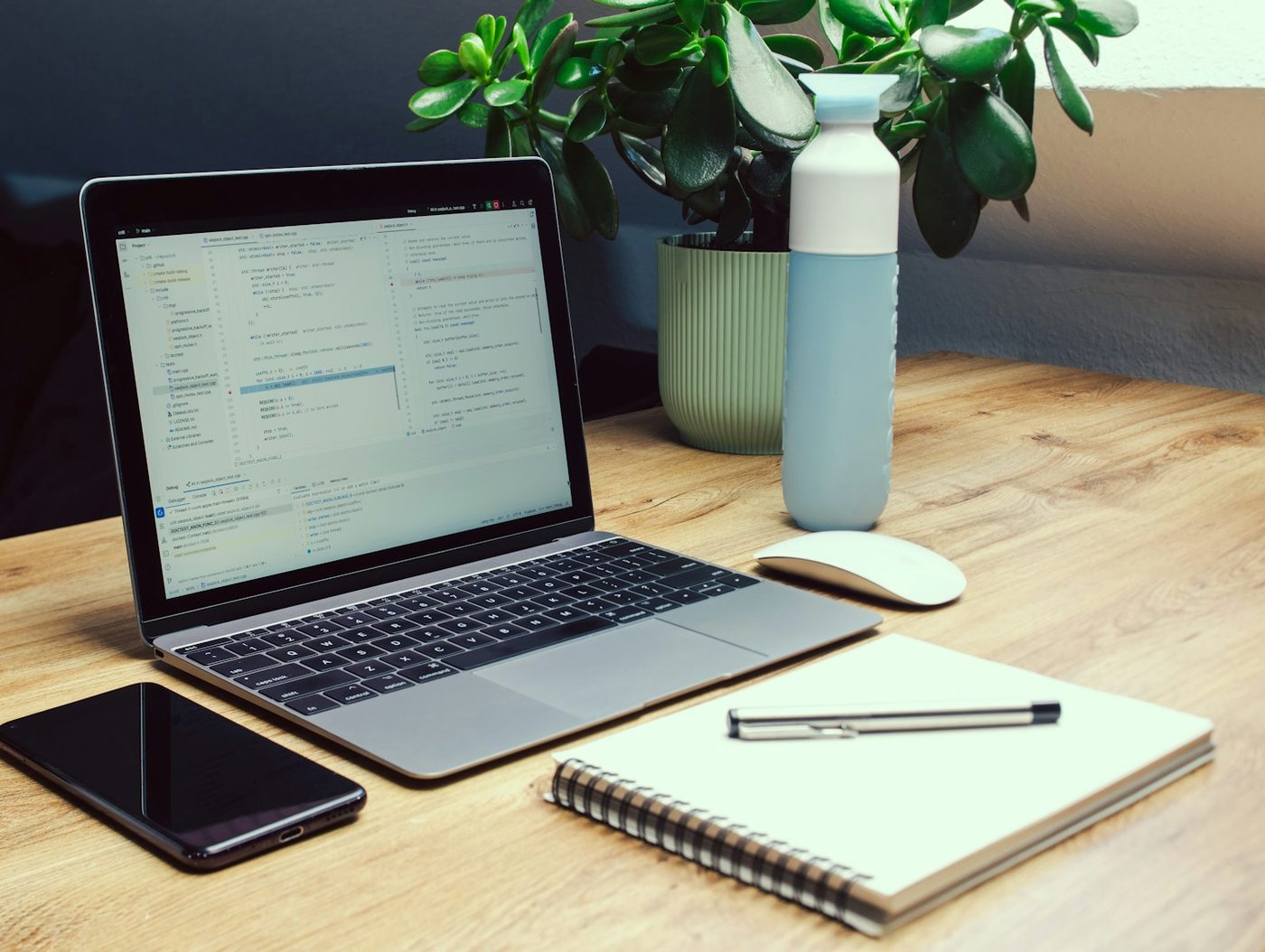 Desk with a notebook, pen, water bottle, phone, and laptop